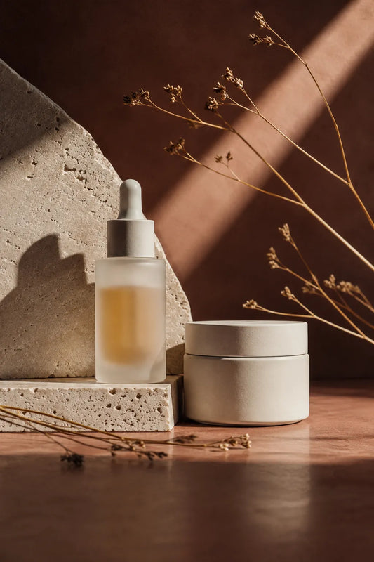 Example output from the Editorial Beauty Product Photos ChatGPT prompt: a luxury editorial skincare product photo with dramatic sunlight, sculptural shadows and a refined minimalist composition of jars and bottles styled with botanicals in muted tones.