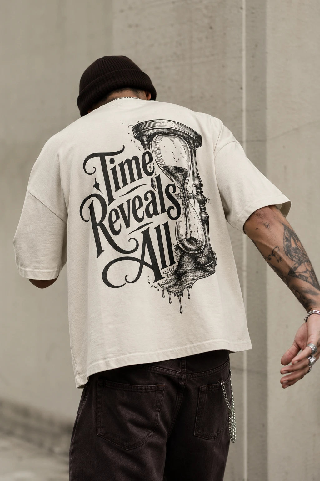 Example output from the Heritage Back Print Tee Designs ChatGPT prompt: a cream oversized tee with a Time Reveals All heritage back print, shot from behind against a concrete backdrop.