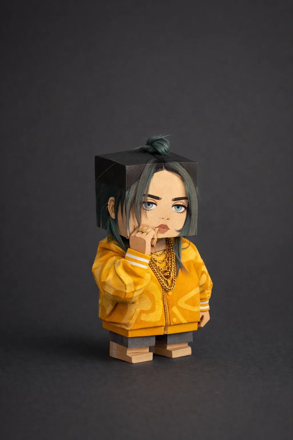 Cube-headed cardboard paper toy character on colorful studio background, showing photo-to-figure style with clean negative space: Billie